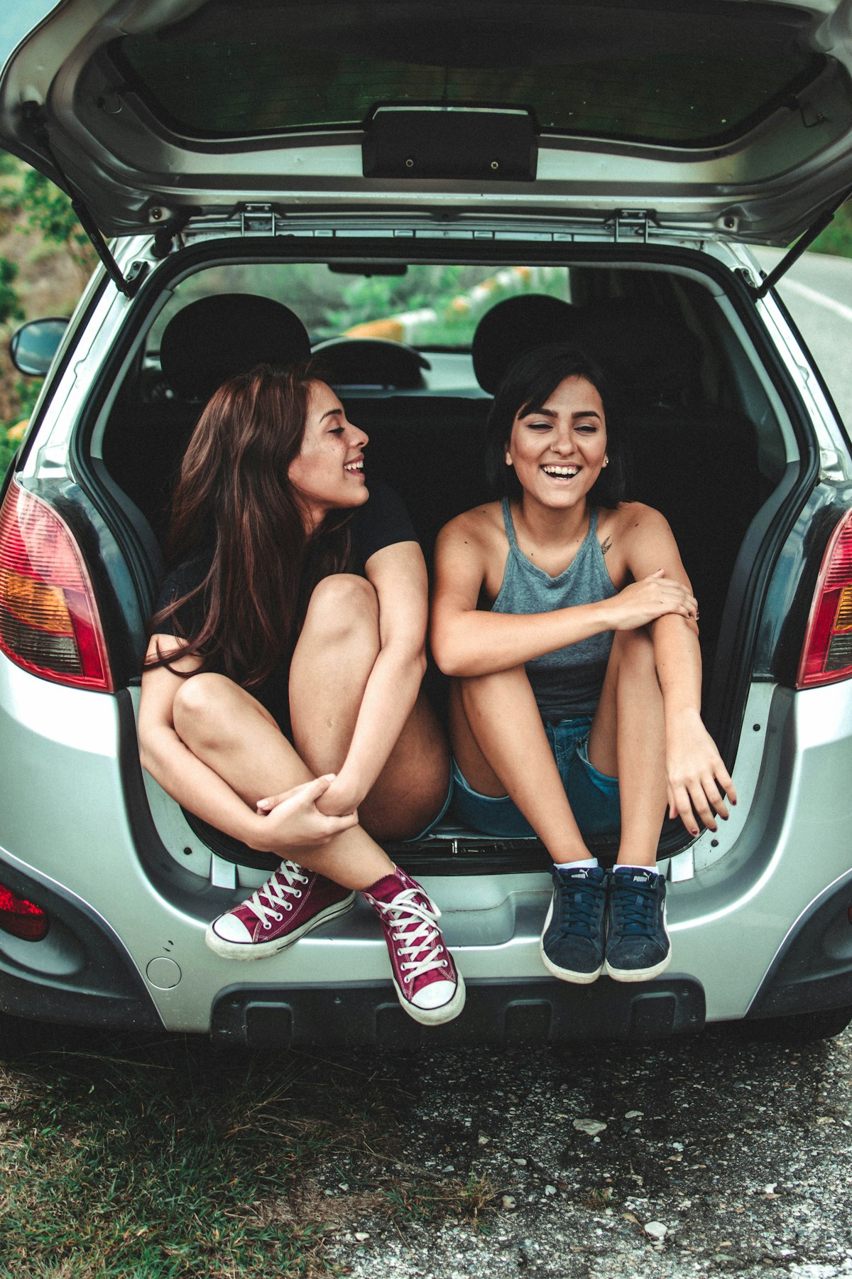 Two people sitting in the back of a hatchback, smiling